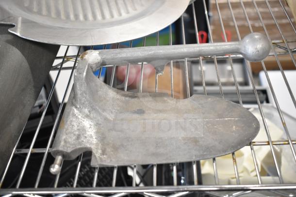 Metal meat slicer arm on wire rack, part of a lot with pelican head and food processor blades, showing moderate wear.