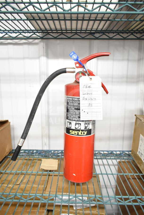 Red Sentry fire extinguisher, brand new, with attached instructional label on metal shelf.