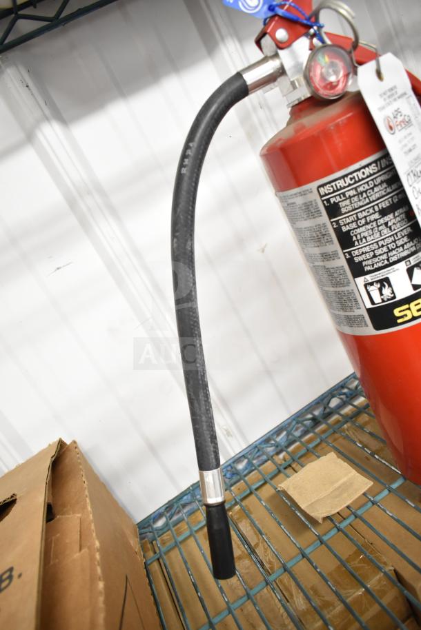 "Brand new Sentry fire extinguisher, red cylinder with attached hose, instructions and safety tag visible."