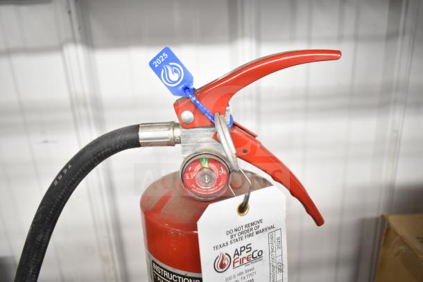 Brand new red Sentry fire extinguisher, safety tag marked 2025, APS FireCo inspection tag attached.