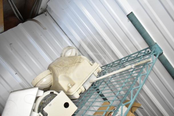 Six various items including a dusty emergency light on a metal shelf. Items show wear; emergency light is beige.
