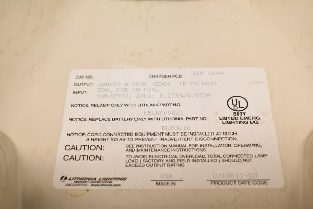 Close-up of Lithonia Lighting emergency light label with specifications: 50W, 120/277V, 60Hz, UL listed. Model details included.