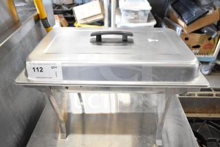 Stainless steel countertop chafer with lid, black handle, and folding legs. Visible label with auction details. Ideal for catering.