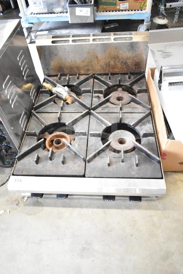 Commercial countertop gas-powered 4 burner range with used black grates, stainless steel front, and visible gas connection.