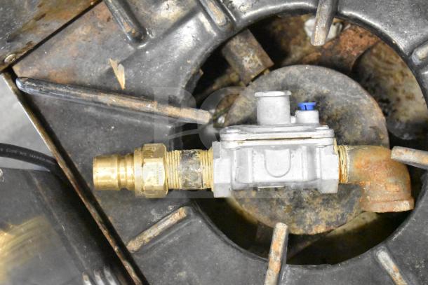 Commercial countertop gas-powered 4 burner range in used condition, featuring a sturdy gas connection fitting, visible rust and wear.