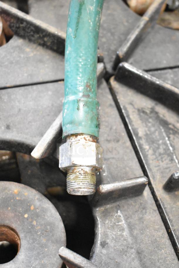 Close-up of a commercial gas-powered 4 burner range, showing rust on the connector and burners, indicating wear.