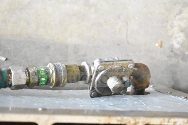 Close-up view of the gas connection of a commercial countertop gas-powered 4 burner range. Pipes show signs of use.