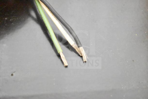 Three exposed copper wires with black, white, and green insulation on a dark surface.