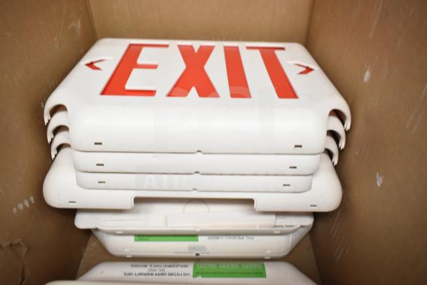 Stack of new DualLite exit signs and remote heads, white with red lettering, in box. Some labels visible. 50 items total.