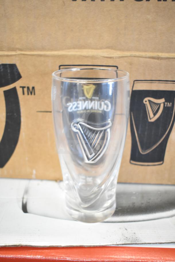 Guinness 16 oz beer glass with embossed harp logo, clear glass, great condition. Background shows packaging with logos.