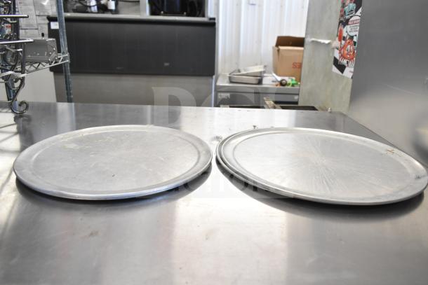 Two round metal trays on a stainless steel countertop; part of a lot including chafing dish frames. Slightly worn condition.