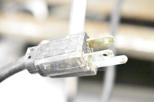 A close-up image of a power cord plug with visible signs of rust and wear, highlighting electrical connection components.