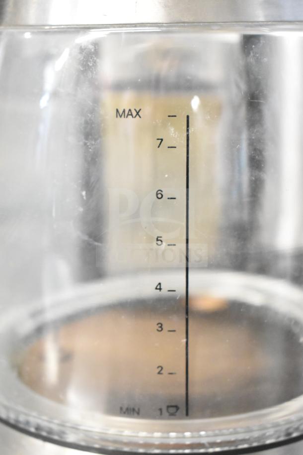 Close-up of a clear container with measurement markings from 1 to 7, indicating capacity levels, part of a kitchen appliance.
