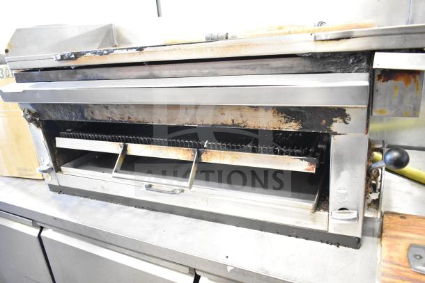 Commercial gas powered flat top griddle with cheese melter, stainless steel, visible wear, ideal for high-volume cooking.