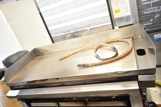 Commercial gas-powered flat top griddle with attached cheese melter, featuring a metallic surface and control knobs. Used condition.