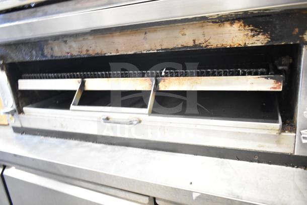 Commercial gas-powered flat top griddle with cheese melter, stainless steel, used condition, showing grill and open drawer.
