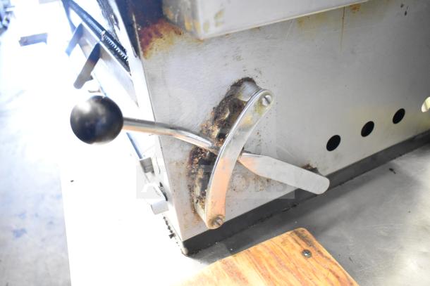 Commercial gas flat top griddle with cheese melter, showing handle and levers. Visible wear and rust, indicating used condition.