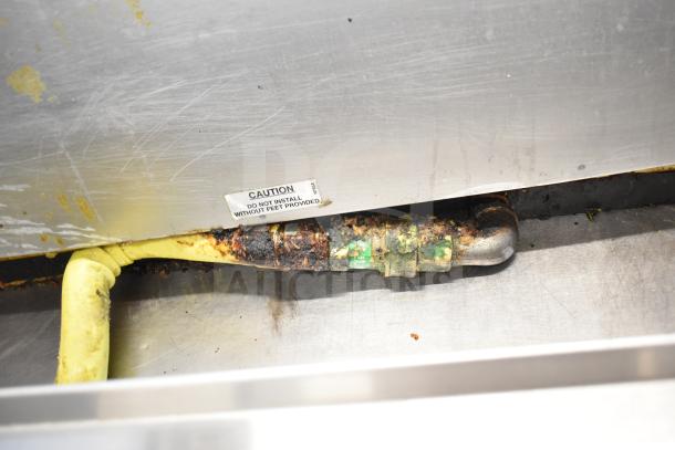 Commercial gas-powered flat top griddle with cheese melter, showing signs of wear; caution label advises installation with feet.