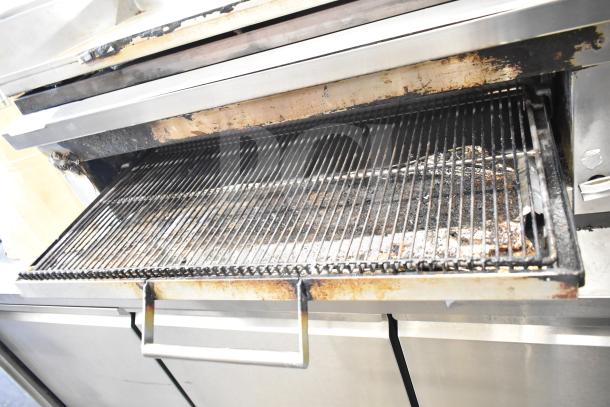 Commercial gas-powered flat top griddle with cheese melter, showing signs of use, featuring a durable metal frame and adjustable grates.