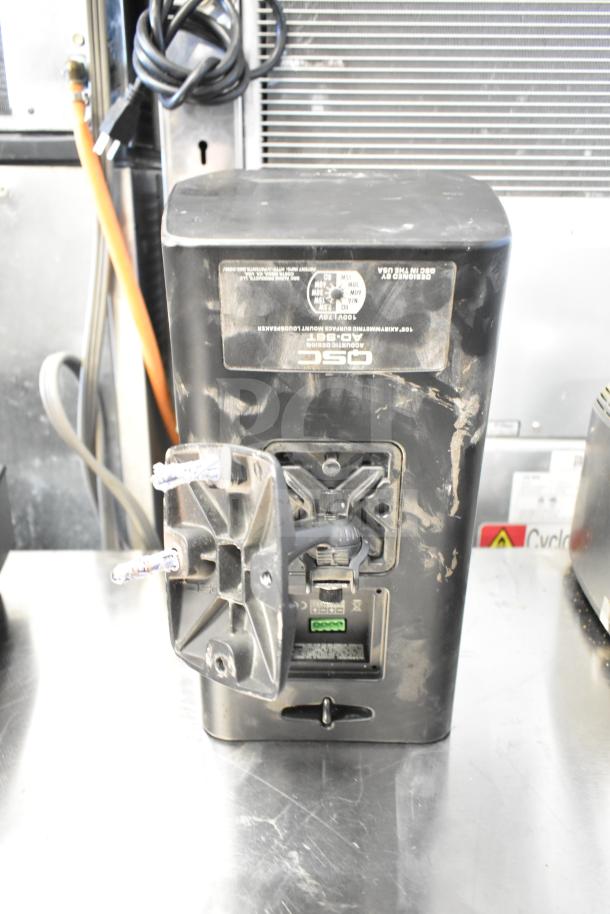 Dusty QSC AD-S6T speaker in used condition, rear view showing mounting bracket and connection panel with visible labels.