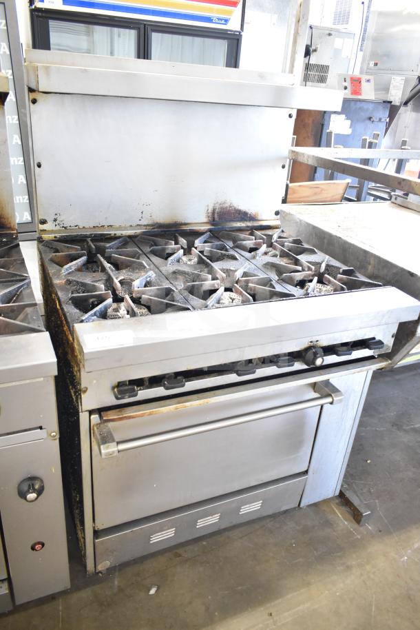 Commercial gas-powered 6 burner range with oven, over shelf, and backsplash. Used condition, visible wear.