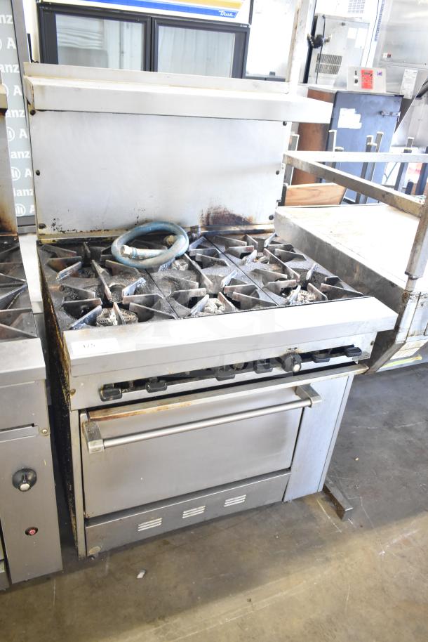 Commercial gas-powered 6 burner range with oven, over shelf, and backsplash. Shows signs of use with visible wear.