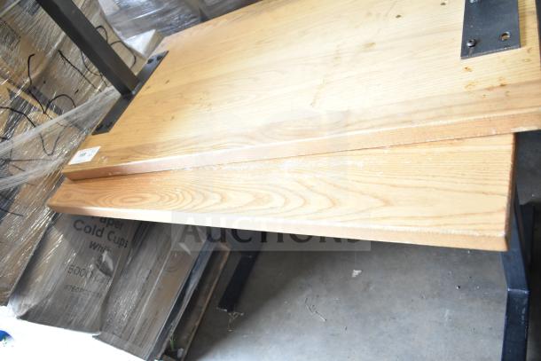 Two wooden dining-height tables with sturdy black metal legs, light wood finish, some wear visible, lot tag attached.