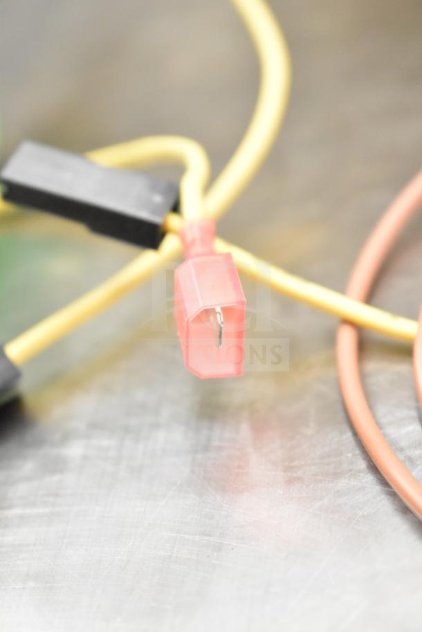 Close-up of a yellow gauge wire with a red connector, showing a single metal prong. Features black and orange wires.