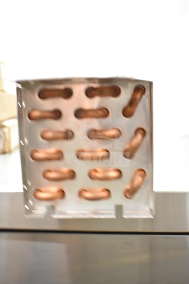 Copper evaporator coil with multiple curved tubes, shown partially enclosed in metal casing, indicative of unused condition.