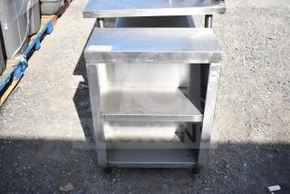 Commercial stainless steel counter with two under shelves, lightly scuffed, suitable for kitchen or storage use.