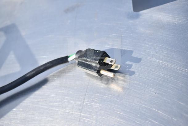 A close-up of a black power plug on a stainless steel surface, showing its three prongs and black power cord.