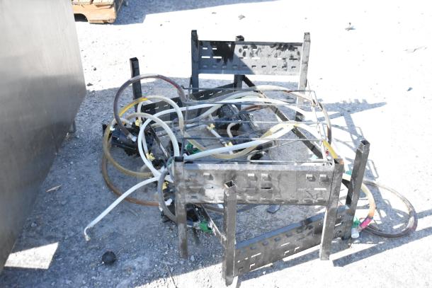 4 soda pumps on black metal soda box rack, used condition, with multiple hoses attached, outdoor setting.