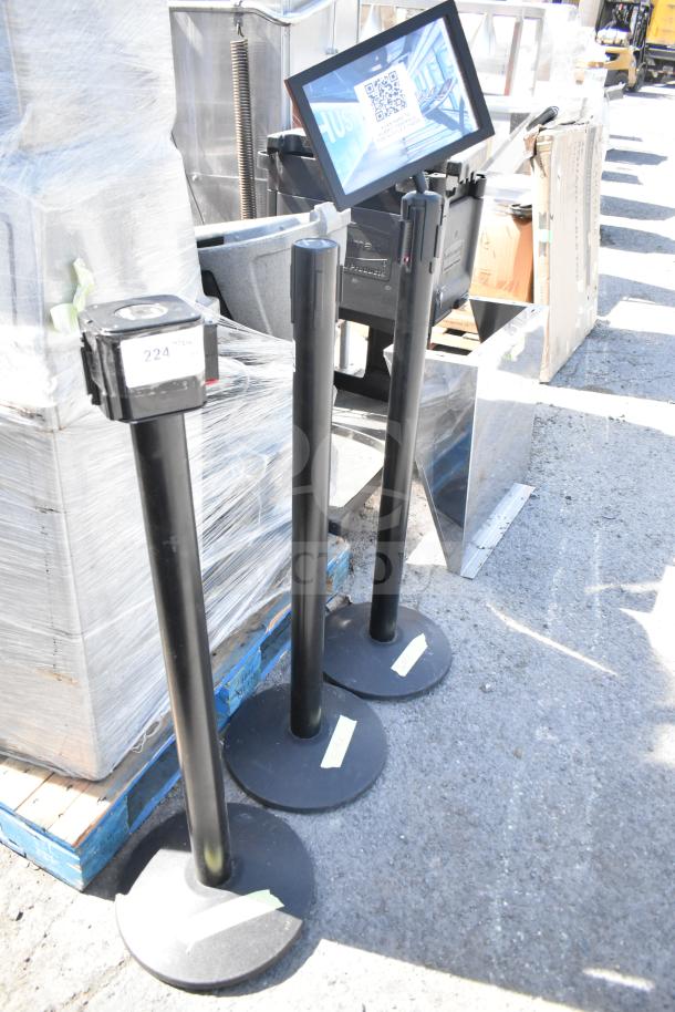 Three black stanchions with round bases, in used condition. Each has a retractable belt. Label reads "224."