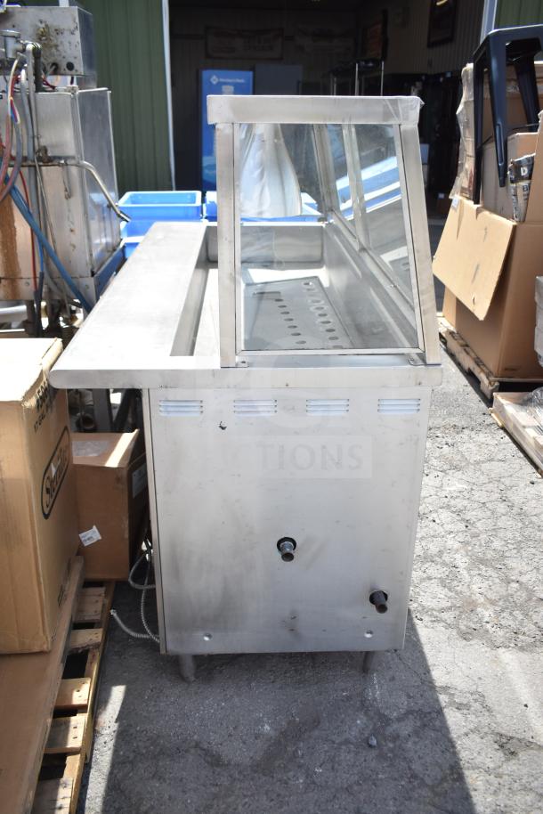 Commercial hot food merchandising case, stainless steel, glass front, well-used condition, ventilation slits, outdoor setting.