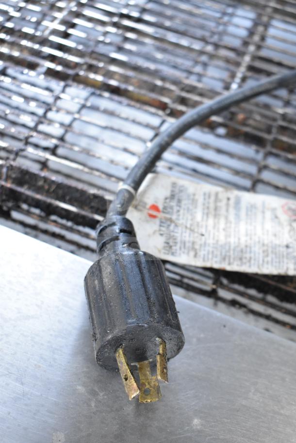Power plug of Middleby Marshall PS638G conveyor pizza oven, resting on metal surface. Label with safety info visible in background.