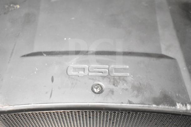 QSC AD-S6T speaker with visible grille and QSC logo on casing, shows signs of use. Includes 7 Crestron SAROS PD6T-B-T-EACH speakers.