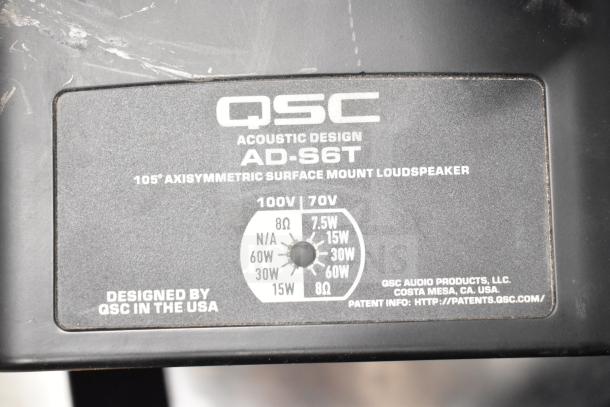 Close-up of QSC AD-S6T speaker label showing model name, 105° axisymmetric design, and 100V/70V power settings.