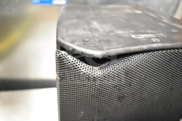 Damaged black speaker with dented mesh grille and worn surfaces, possibly QSC AD-S6T or Crestron SAROS PD6T-B-T-EACH model.