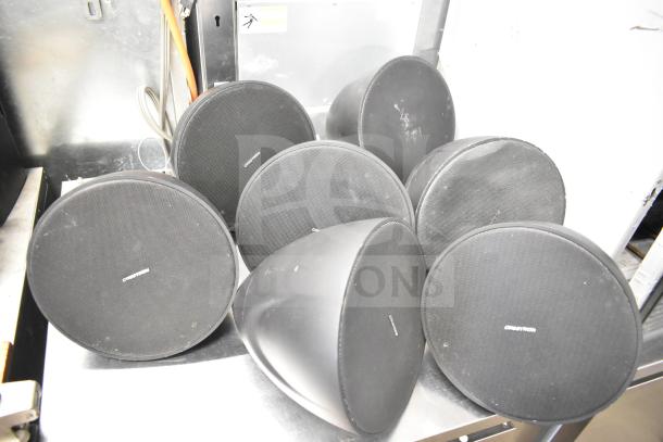 8 speakers including 1 QSC AD-S6T and 7 Crestron SAROS PD6T-B-T-EACH, showing front grills and brand logos.