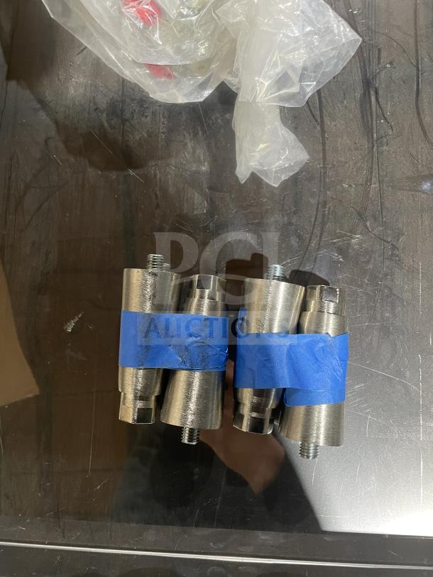 Stainless steel connectors with blue tape, on a reflective surface, next to plastic packaging.