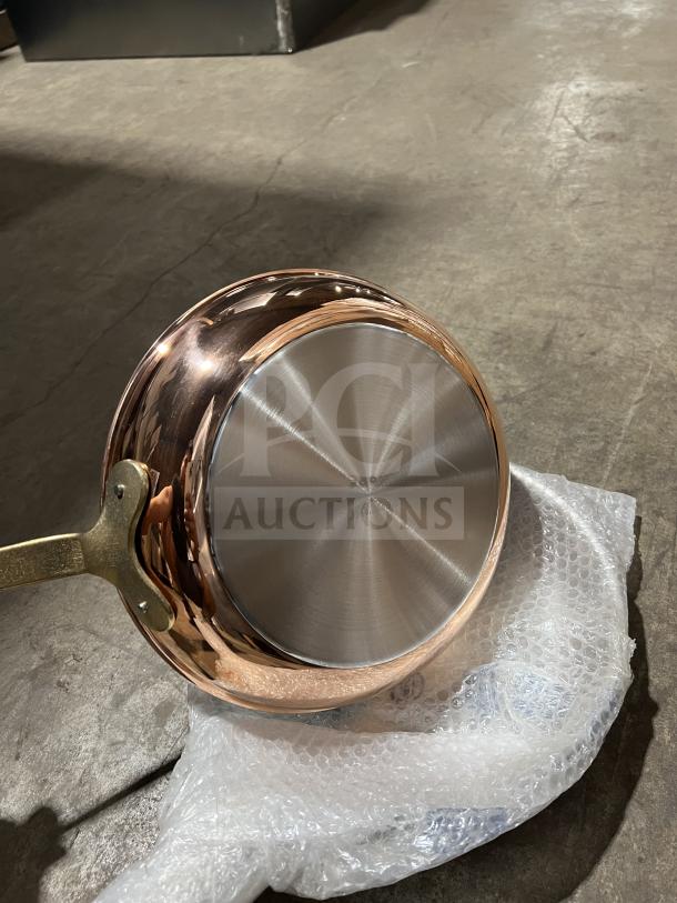 Brand new commercial stainless steel frying pan with a brass handle, reflective finish, packaged in bubble wrap.