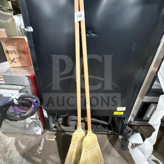 Two new wooden corn brooms with natural bristles, standing upright. Auction tag marked "148".