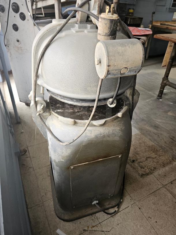 Commercial dough divider, metallic gray, used condition with visible dust. Features a round top and electrical components.