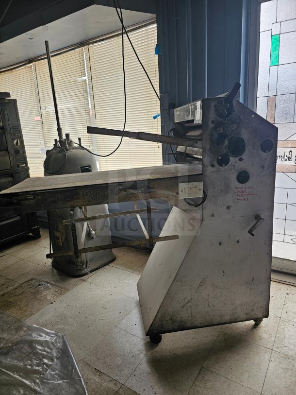 Commercial dough sheeter in used condition, features rollers and manual adjustment knobs. Visible wear indicates frequent use.