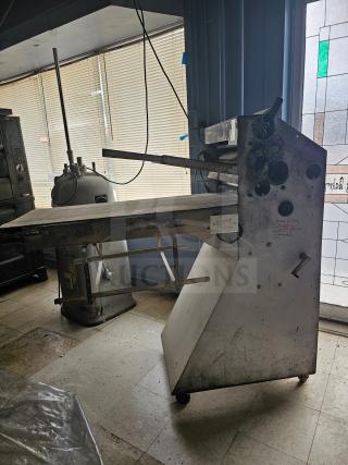 Commercial dough sheeter in used condition, features rollers and manual adjustment knobs. Visible wear indicates frequent use.