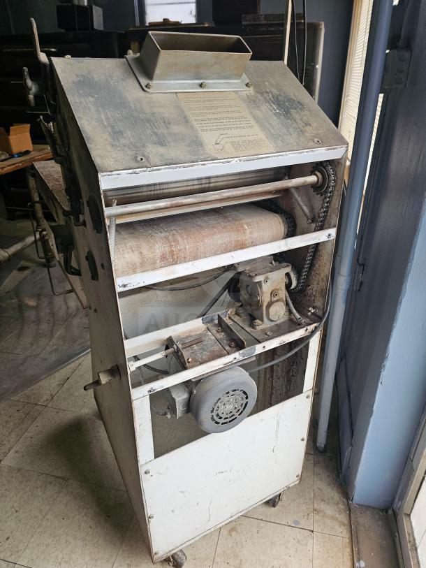 Commercial dough sheeter, metal construction, used condition; features rollers and motor, visible instructions on top panel.