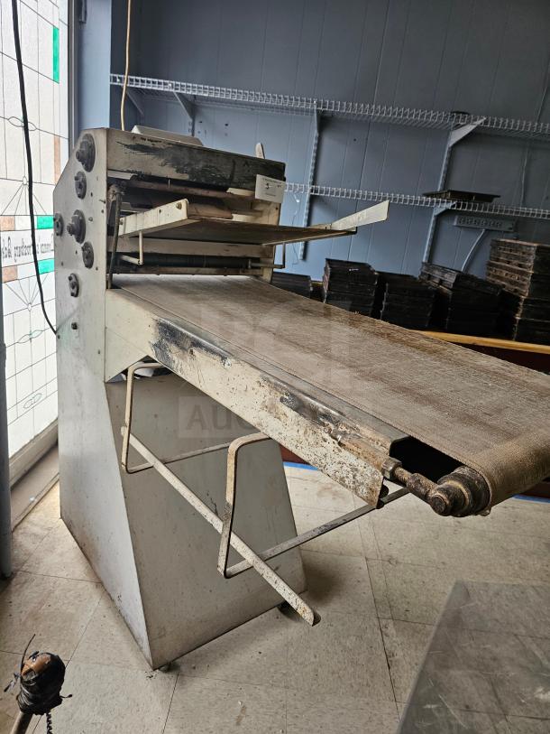 Commercial dough sheeter in used condition, featuring a conveyor belt, control knobs, and metal structure with wear and rust.