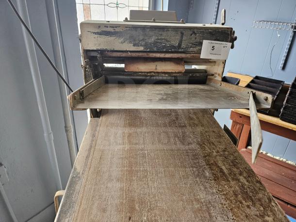 Commercial dough sheeter with worn surface, metal frame, and rollers. Visible label marked "5 QTY" for auction details.