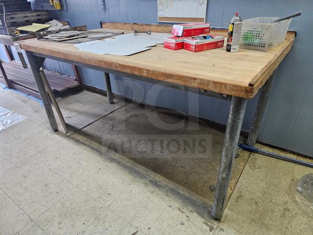Wood top work table with metal legs, sturdy design. Features a spacious tabletop with slight wear, ideal for workshops.
