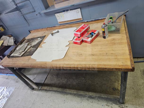 Wood top work table with metal legs, showing minor wear. Includes items like vinyl glove boxes and a spray can on top.